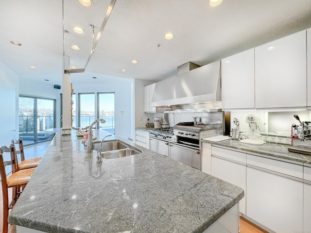 kitchen with a water view, sink, a center island with sink, and exhaust hood