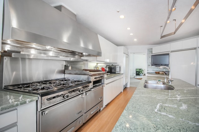 kitchen featuring wall chimney exhaust hood, sink, light stone counters, light wood-type flooring, and white cabinets