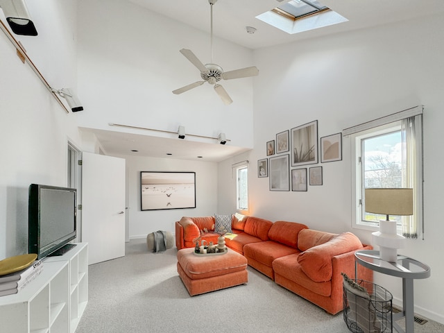 living room with light carpet, a skylight, ceiling fan, and a high ceiling