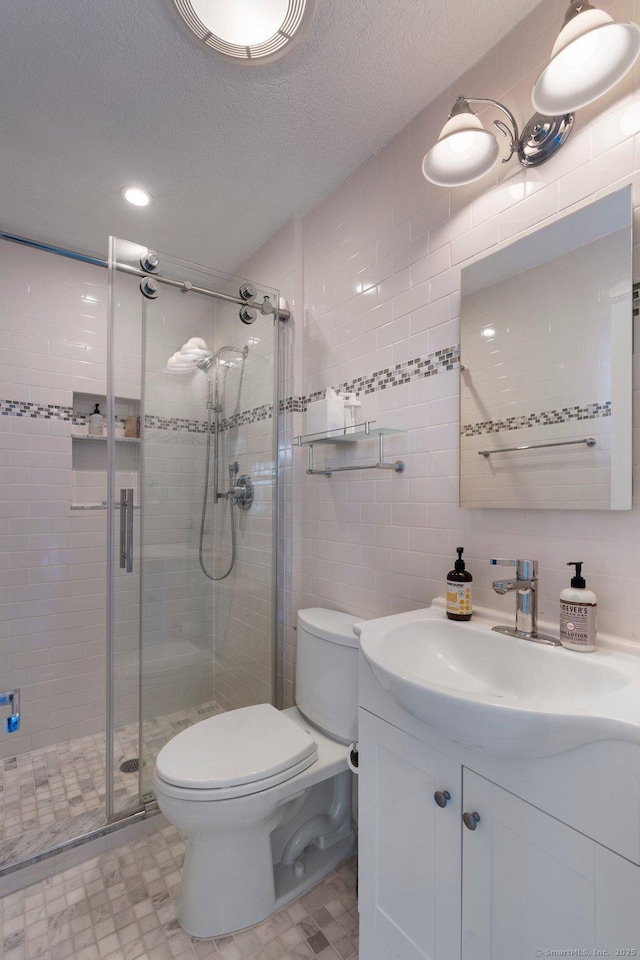 bathroom featuring toilet, a shower with shower door, a textured ceiling, tile walls, and vanity