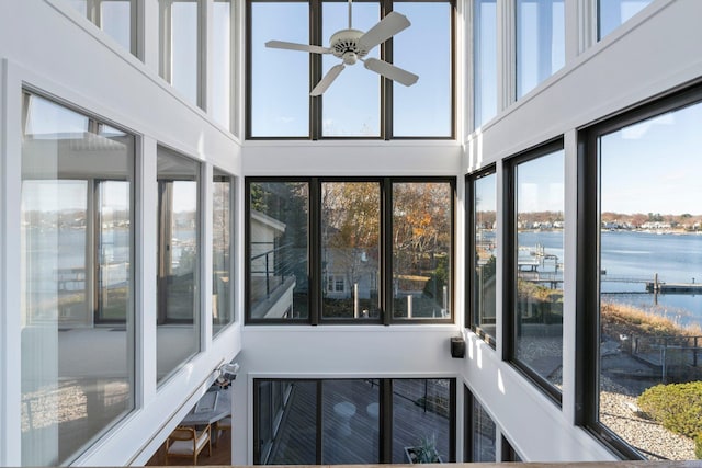 unfurnished sunroom with ceiling fan and a water view