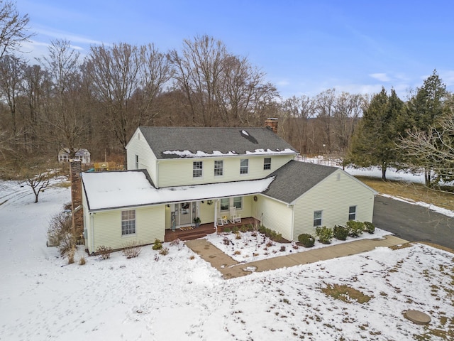 snow covered back of property featuring covered porch