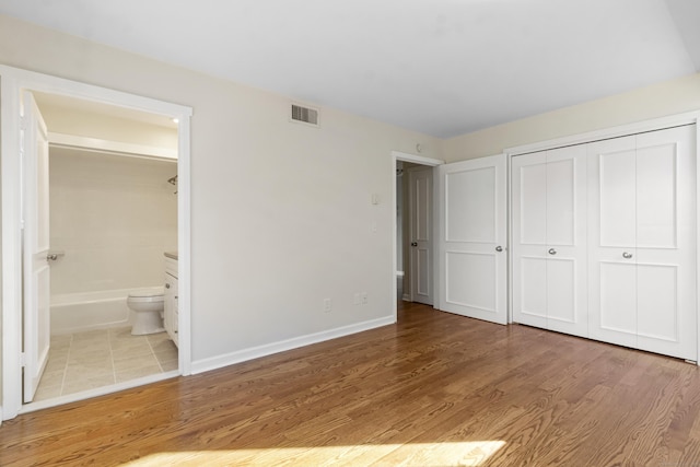 unfurnished bedroom featuring ensuite bathroom, light wood-type flooring, and a closet