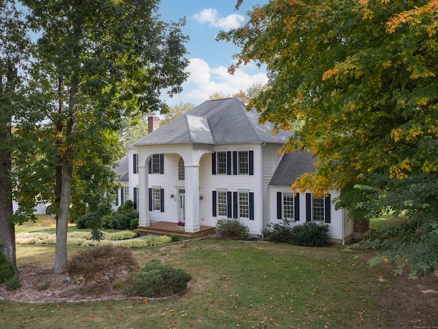 view of front of house featuring a front lawn, a chimney, and a shingled roof