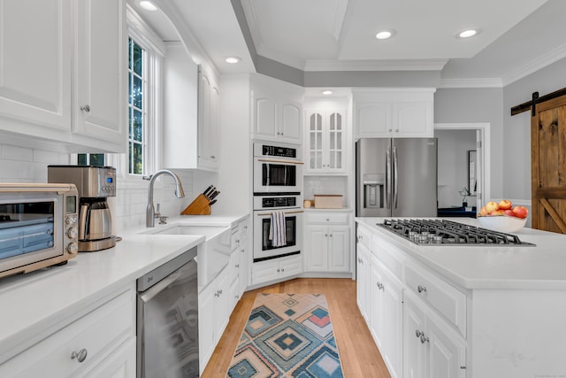 kitchen with a barn door, white cabinets, light countertops, appliances with stainless steel finishes, and glass insert cabinets