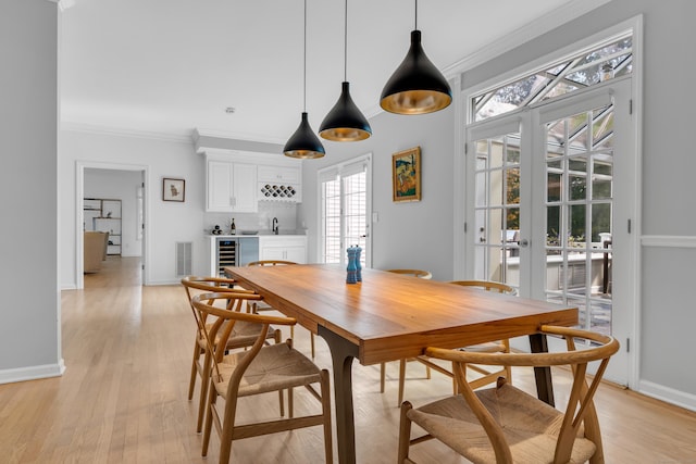 dining space featuring light wood-type flooring, crown molding, and indoor wet bar