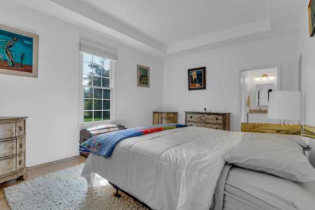 bedroom featuring wood-type flooring, a raised ceiling, and ensuite bathroom