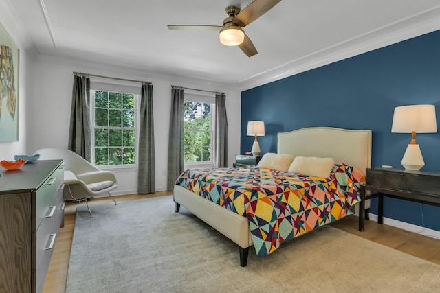 bedroom featuring ornamental molding, light wood-type flooring, a ceiling fan, and baseboards