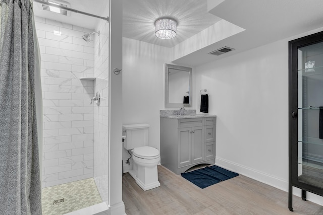 full bathroom featuring baseboards, toilet, wood finished floors, a tile shower, and vanity