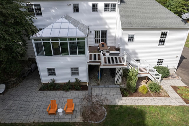 back of property with a deck, a patio, a shingled roof, a sunroom, and stairway