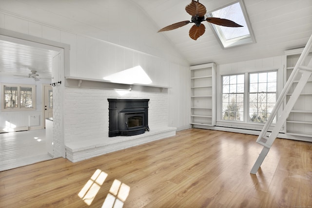 unfurnished living room featuring vaulted ceiling with skylight, hardwood / wood-style floors, ceiling fan, and built in shelves