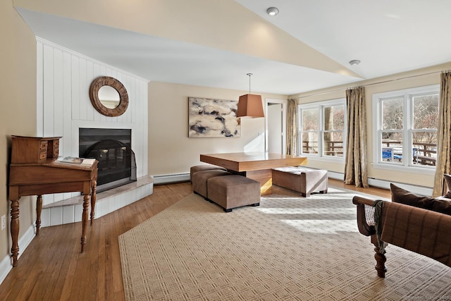 living room featuring light hardwood / wood-style flooring, a baseboard heating unit, vaulted ceiling, and a large fireplace