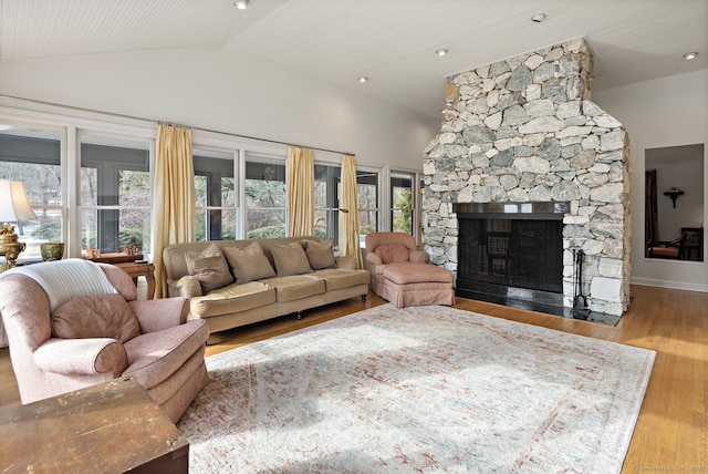 living room featuring a stone fireplace, vaulted ceiling, light hardwood / wood-style floors, and a wealth of natural light