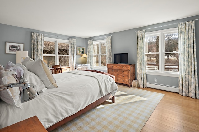 bedroom featuring light wood-type flooring, multiple windows, and a baseboard heating unit