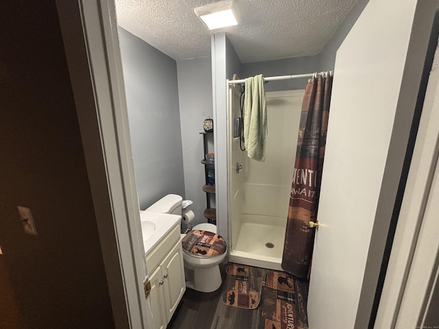 bathroom featuring a textured ceiling, toilet, wood finished floors, vanity, and a stall shower