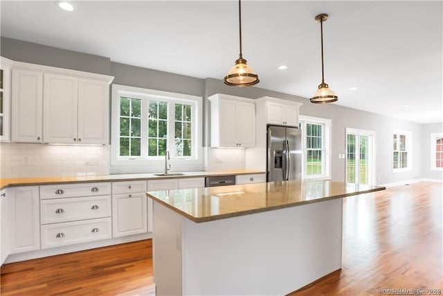 kitchen with sink, appliances with stainless steel finishes, pendant lighting, light stone countertops, and white cabinets