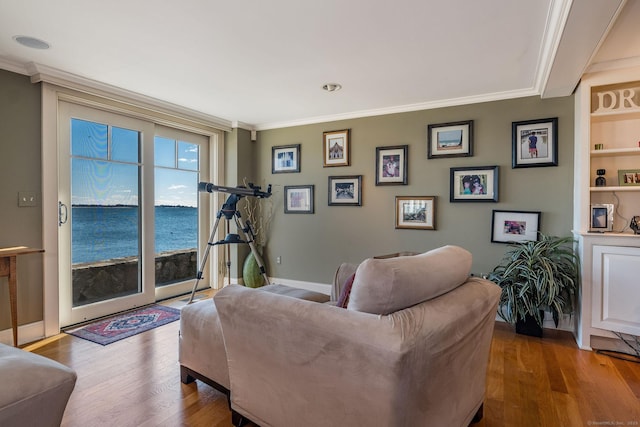 living room featuring crown molding, a water view, hardwood / wood-style floors, and built in features