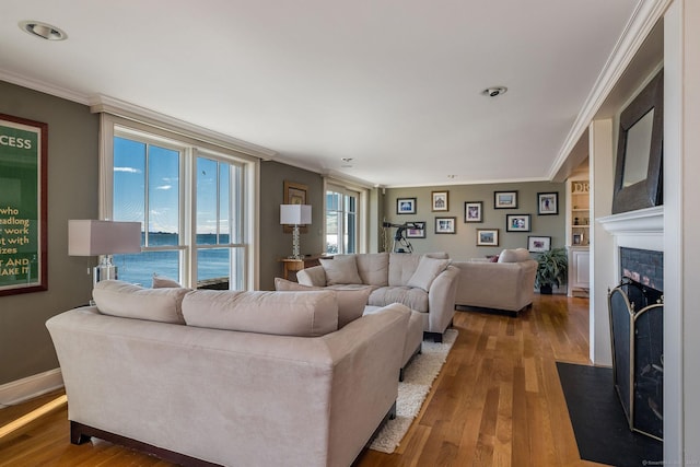 living room featuring wood-type flooring, a water view, crown molding, and built in shelves