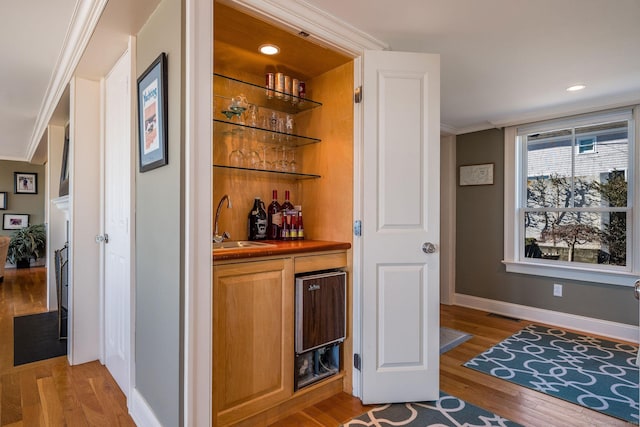 bar with ornamental molding, sink, and light wood-type flooring