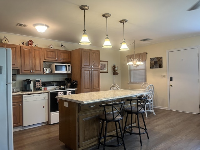 kitchen featuring dark wood-type flooring, a kitchen bar, hanging light fixtures, a kitchen island, and white appliances