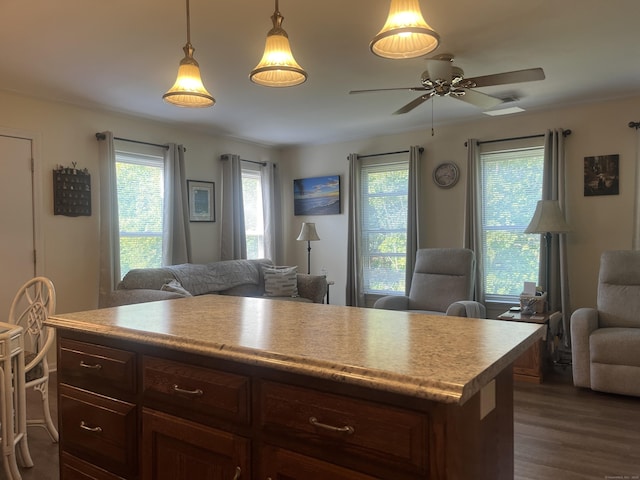 kitchen featuring dark wood-type flooring, dark brown cabinetry, a kitchen island, pendant lighting, and ceiling fan