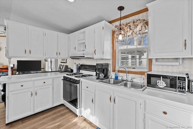 kitchen with sink, light hardwood / wood-style flooring, hanging light fixtures, white cabinets, and white gas range