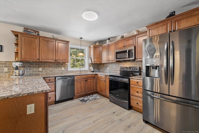 kitchen featuring sink, light stone counters, decorative light fixtures, light wood-type flooring, and appliances with stainless steel finishes