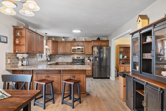 kitchen with a kitchen bar, light hardwood / wood-style flooring, kitchen peninsula, pendant lighting, and stainless steel appliances