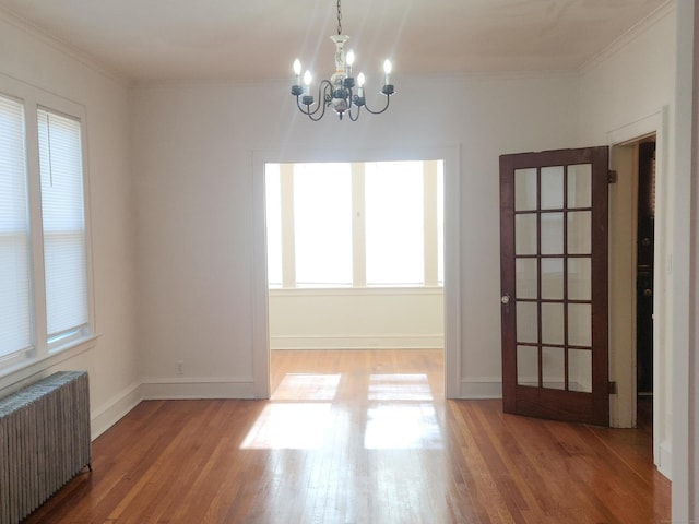 unfurnished room featuring wood-type flooring, radiator, an inviting chandelier, and crown molding