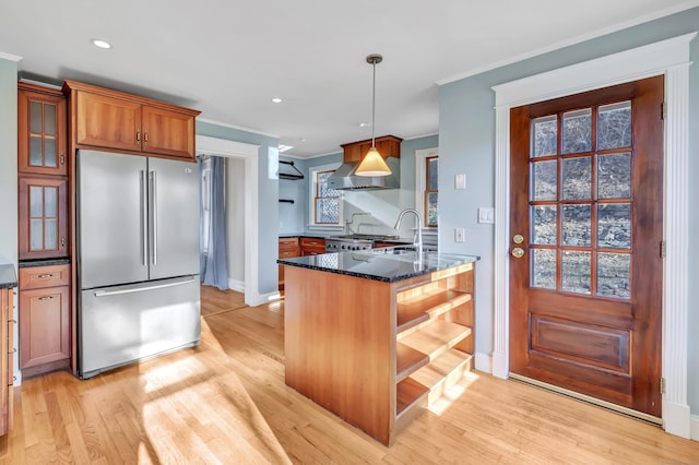 kitchen with hanging light fixtures, light wood-type flooring, stainless steel refrigerator, dark stone counters, and wall chimney range hood