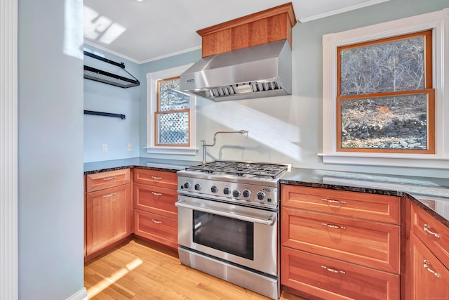 kitchen featuring wall chimney range hood, dark stone countertops, ornamental molding, light hardwood / wood-style floors, and stainless steel range with gas cooktop