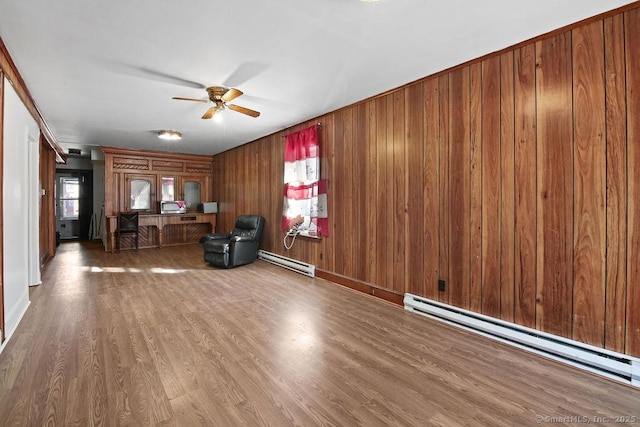 unfurnished living room featuring baseboard heating, ceiling fan, wood-type flooring, and wood walls