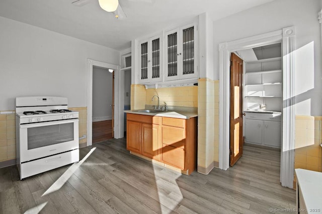 kitchen with white gas range, sink, decorative backsplash, ceiling fan, and light hardwood / wood-style floors