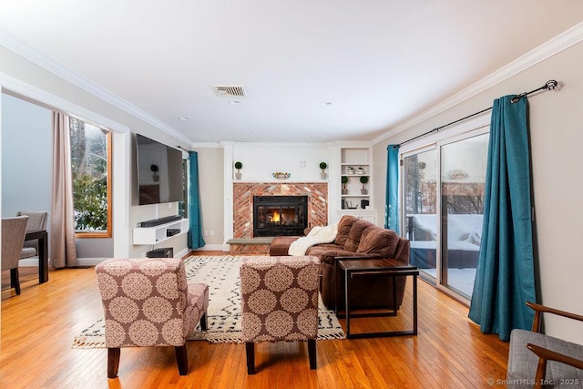 living room featuring crown molding, built in features, a premium fireplace, and light wood-type flooring