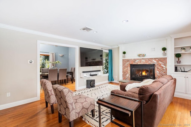 living room with a premium fireplace, crown molding, built in features, and light hardwood / wood-style floors