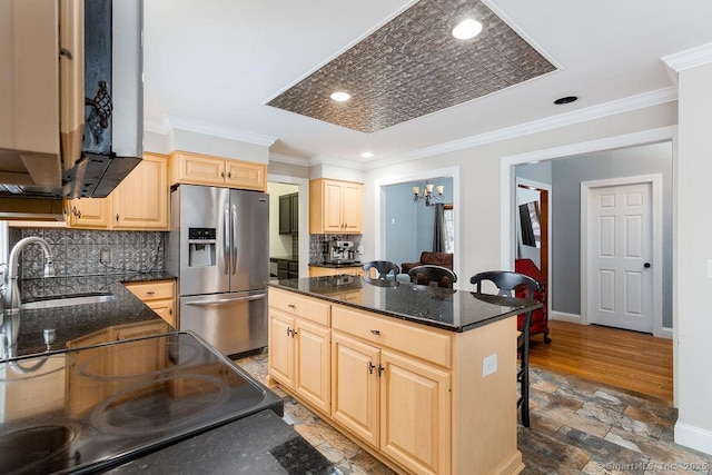 kitchen with sink, a center island, stainless steel refrigerator with ice dispenser, light brown cabinetry, and dark stone counters