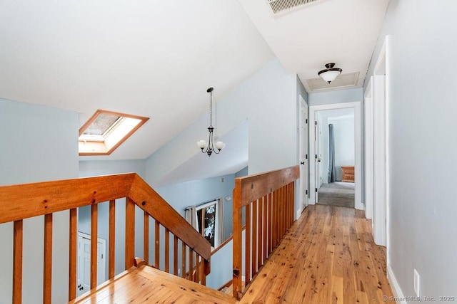 hall featuring an inviting chandelier, lofted ceiling with skylight, and light wood-type flooring