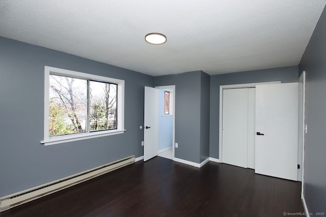 unfurnished bedroom with baseboard heating, a closet, dark hardwood / wood-style floors, and a textured ceiling