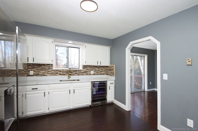 kitchen with dark wood-type flooring, sink, white cabinets, beverage cooler, and backsplash