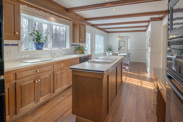 kitchen featuring sink, light wood-type flooring, a kitchen island, pendant lighting, and black appliances