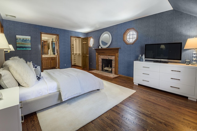 bedroom featuring ensuite bath, dark hardwood / wood-style floors, vaulted ceiling, and a brick fireplace