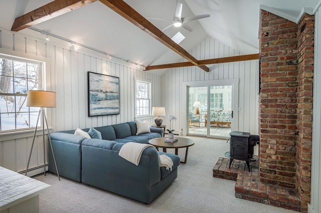 carpeted living room featuring ceiling fan, a baseboard heating unit, track lighting, lofted ceiling with beams, and a wood stove