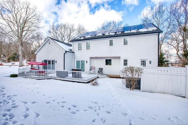 snow covered rear of property featuring a deck and roof mounted solar panels