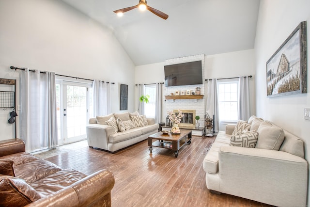 living area featuring a healthy amount of sunlight, a brick fireplace, high vaulted ceiling, and wood finished floors