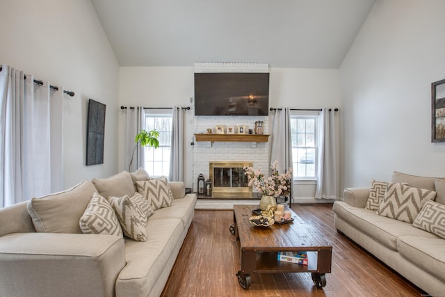 living room featuring dark wood-style floors, high vaulted ceiling, a brick fireplace, and baseboards