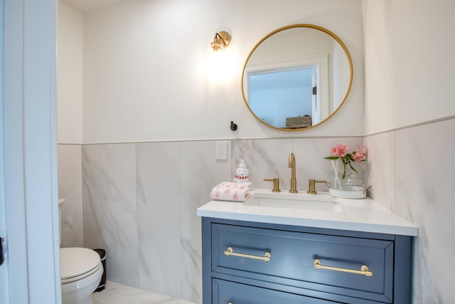 bathroom featuring tile walls, wainscoting, vanity, and toilet