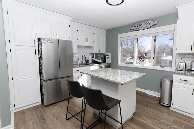 kitchen with light hardwood / wood-style flooring, stainless steel fridge, backsplash, white cabinets, and a kitchen island