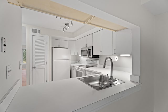 kitchen featuring rail lighting, sink, kitchen peninsula, white appliances, and white cabinets