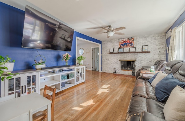 living room with hardwood / wood-style flooring, ceiling fan, brick wall, and a fireplace