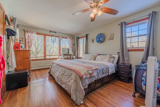 bedroom with multiple windows, hardwood / wood-style flooring, ceiling fan, and baseboard heating